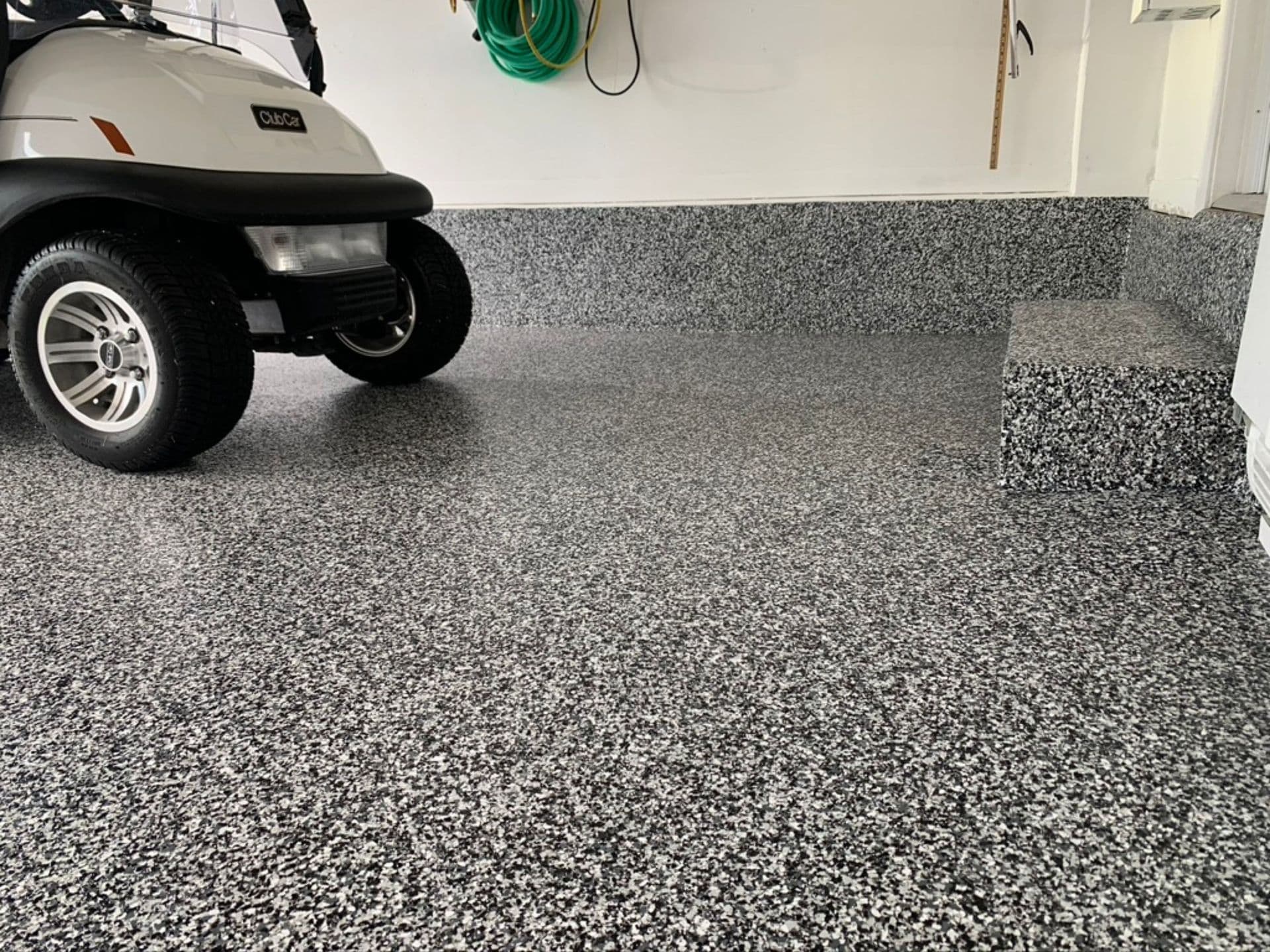 A garage interior with a decorative black and grey flake floor coating, featuring a parked golf cart and coated concrete steps.