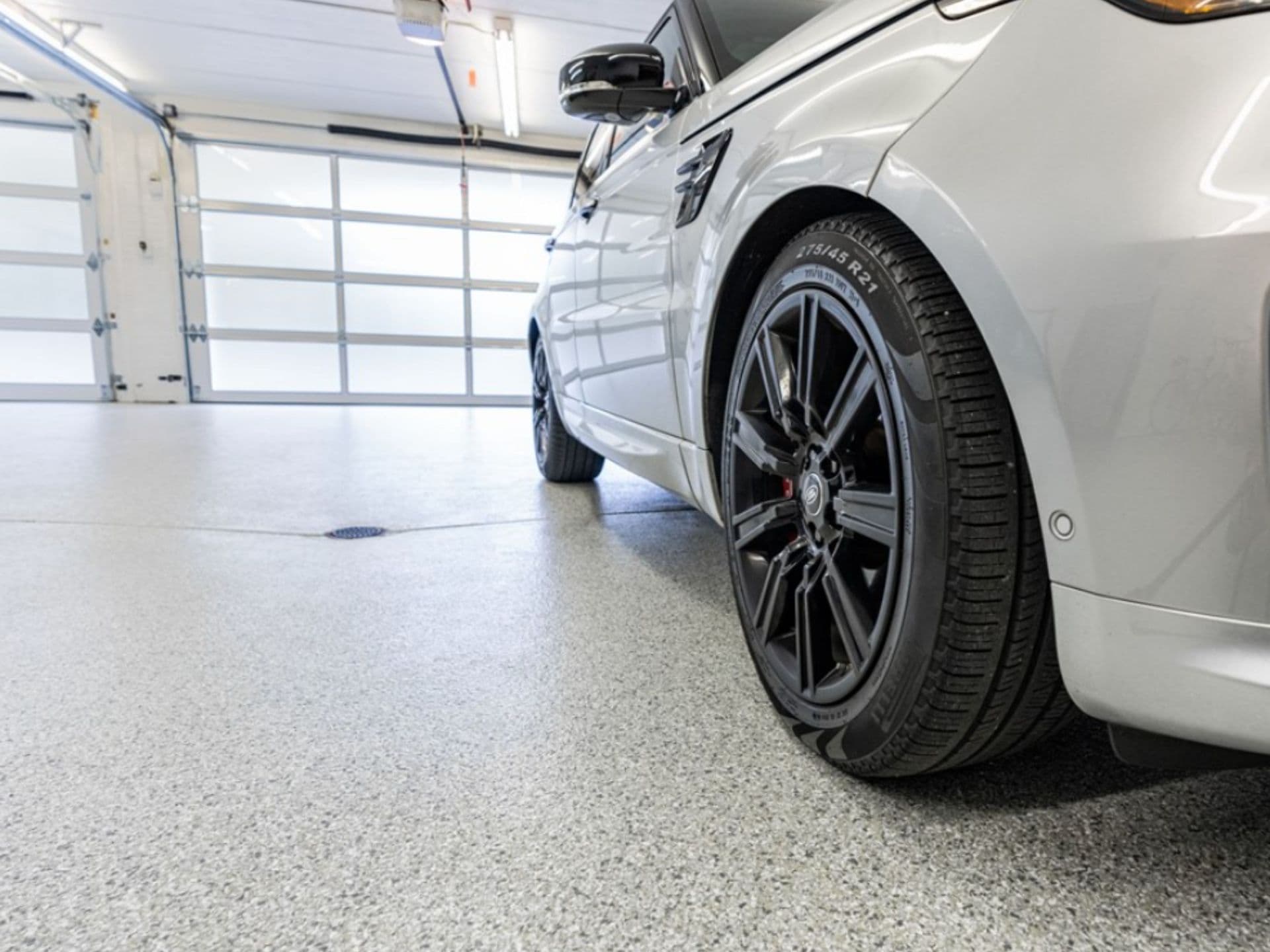 A premium flake-texture polyaspartic garage floor coating beneath a parked silver luxury vehicle.