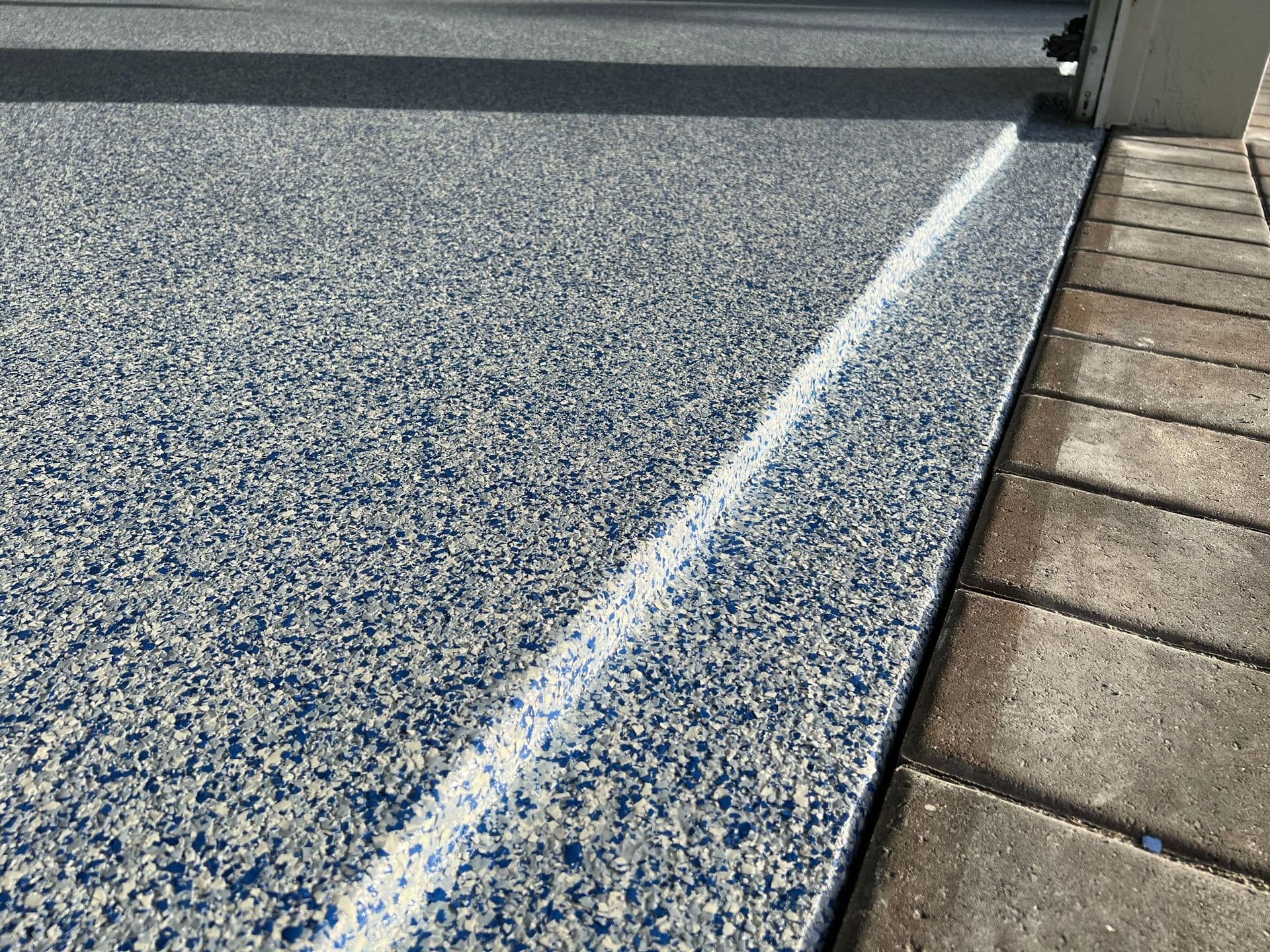A textured, multi-colored polyaspartic concrete floor coating on a garage floor next to brick pavers.